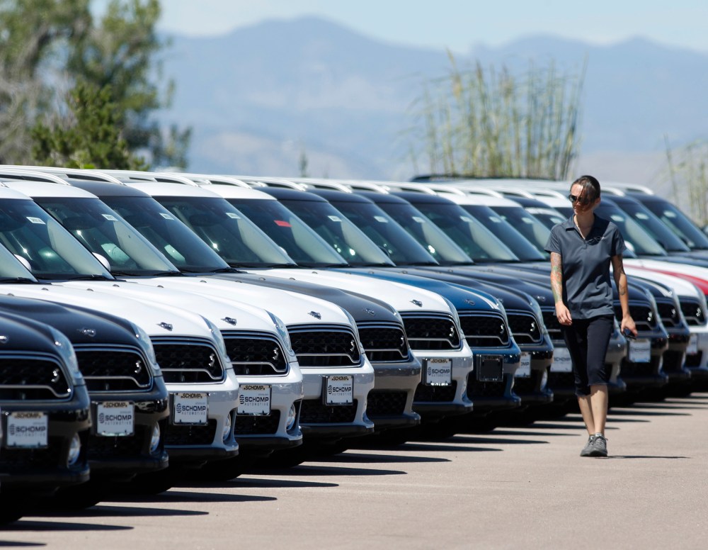 A lot technician passes by a long line of unsold cars at a dealership in Highlands Ranch
