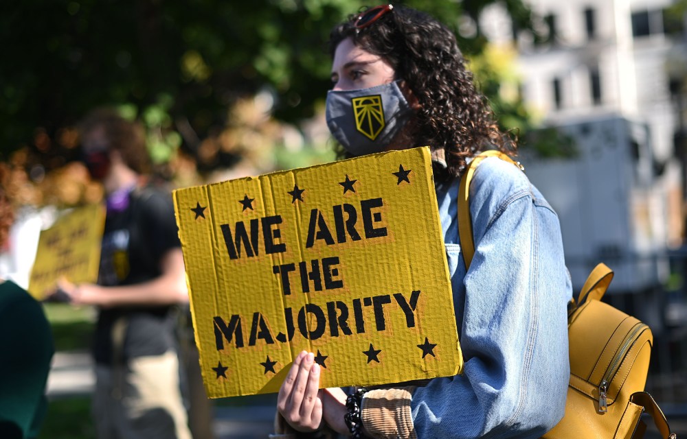 Image: A girl holds a yellow placard that reads,"We are the majority".