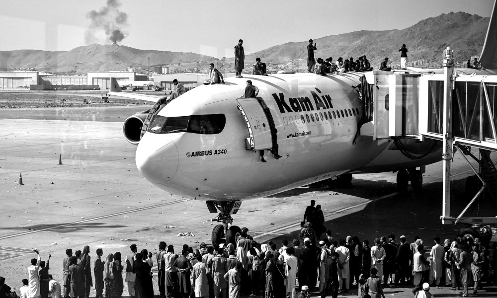 Image: Afghan people climb atop a plane as they wait at the Kabul airport.