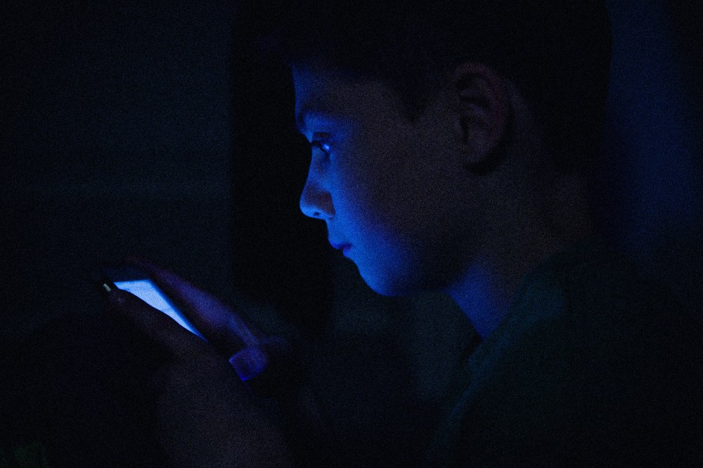 IMage: a teenage boy on his phone, face illuminated in the dark