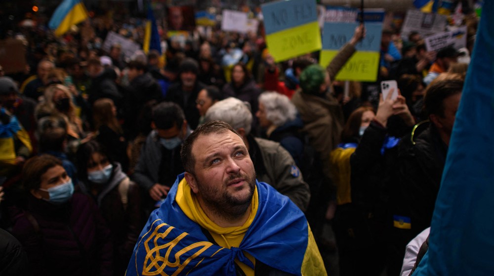 Image: A protestor wearing the colors of the Ukrainian flag looking up.