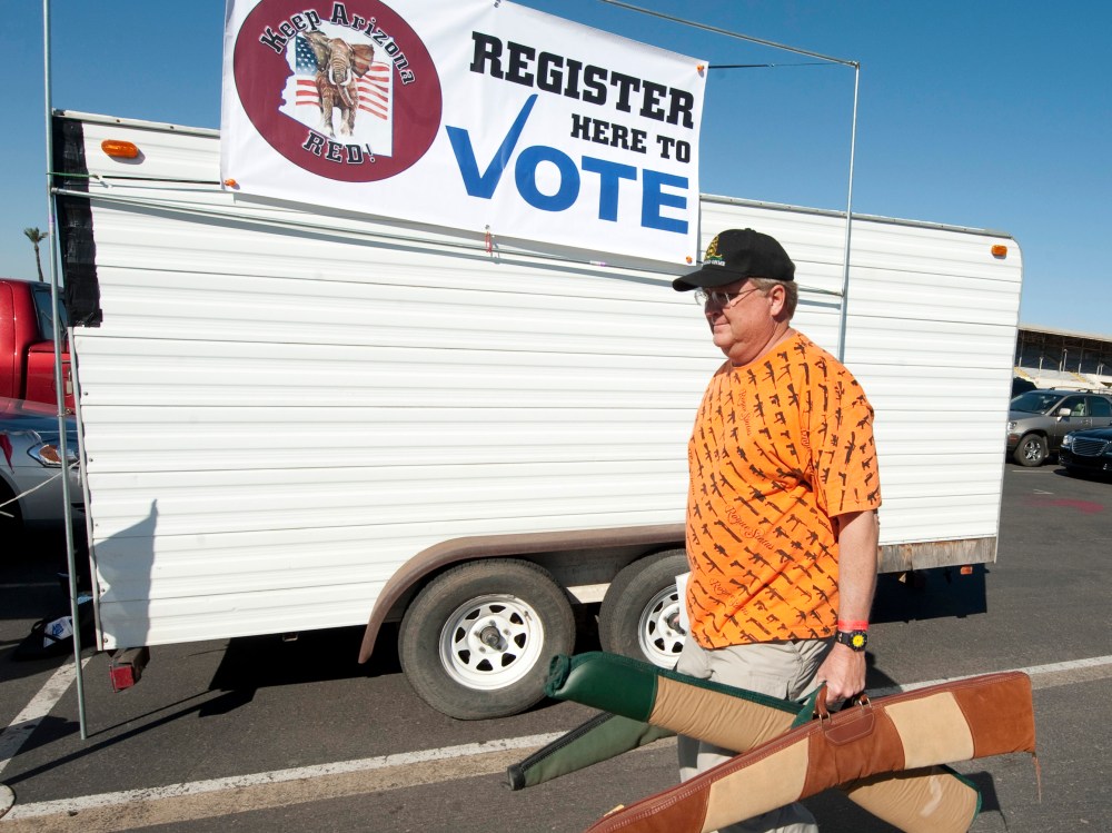 File Photo: A man carries his guns past a voter registration booth on his way to a gun show at the Arizona state fairgrounds February 25, 2012 in Phoenix, Arizona. The Arizona and Michigan primaries are scheduled to be held February 28, 2012. (Photo...