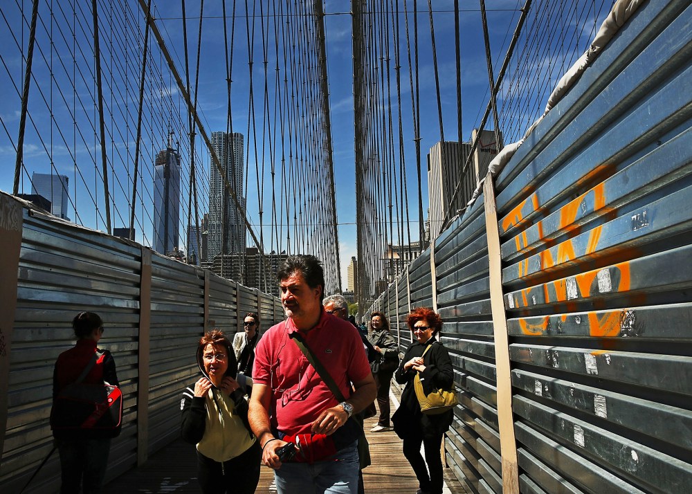People walk past protective metal sheeting along the Brooklyn Bridge on April 30, 2013 in New York City.