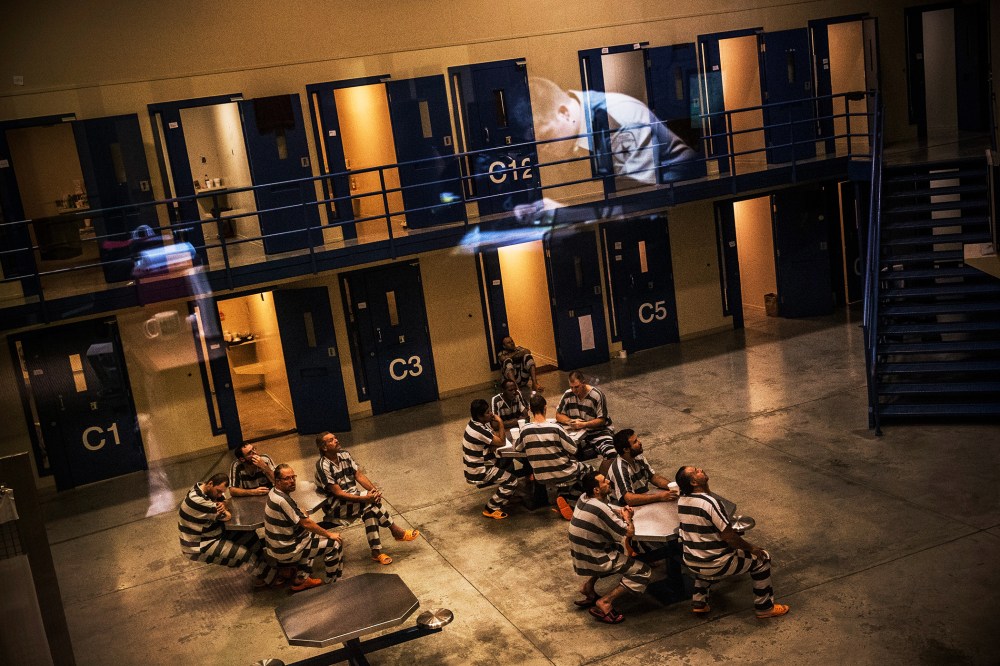 An officer is reflected in the glass as inmates sit in the county jail in Williston, North Dakota, July 26, 2013.