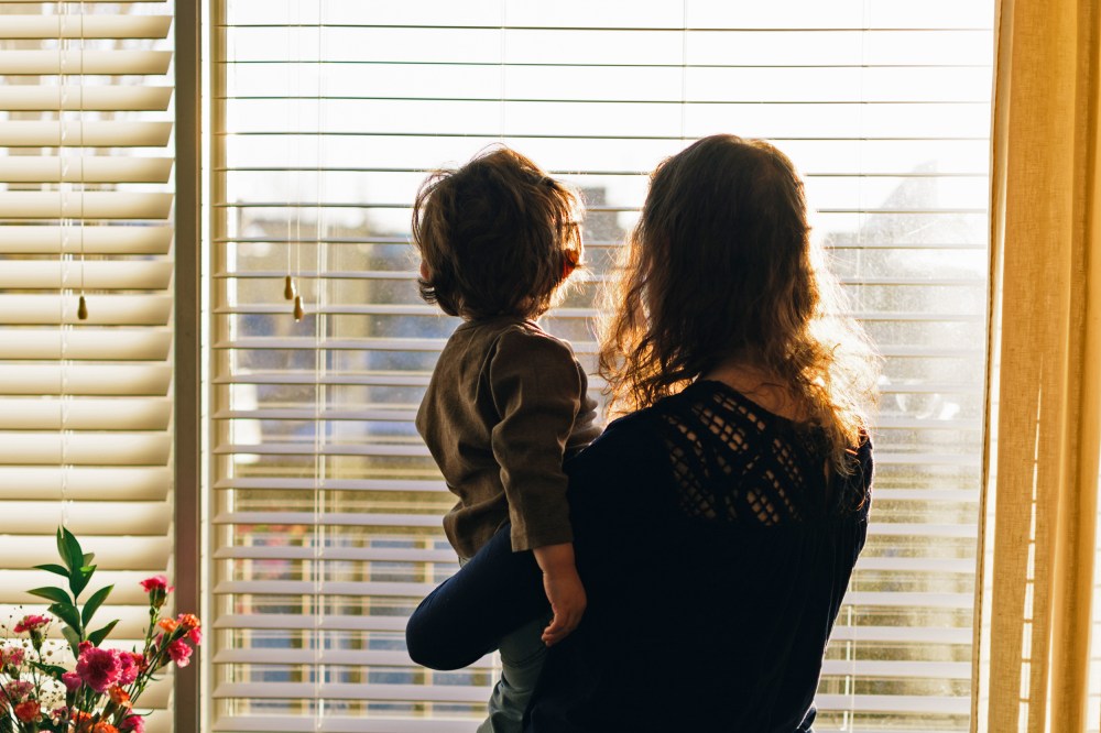 Rear View Of Mother And Baby Standing Against Window