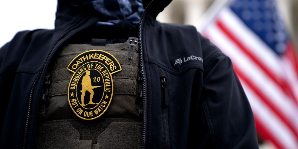 Image: A demonstrator wearing a badge over a protective vest that reads,"Oath Keepers. Guardians of the Republic. Not on our watch."