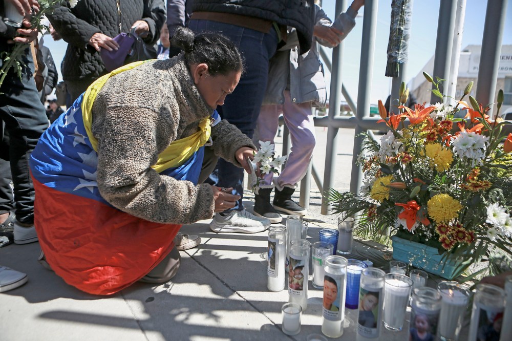 A woman places flowers in front of a gate that has been converted into a memorial outside a Mexican immigration detention center
