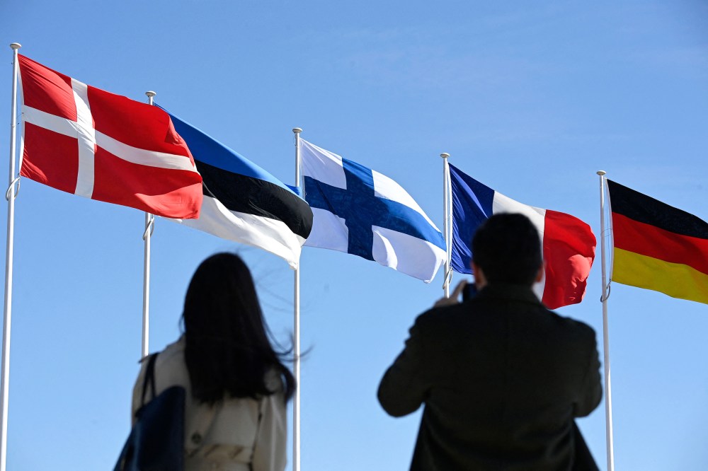 People stand in front of the Finnish national flag, center, after a flag-raising ceremony at the NATO headquarters in Brussels