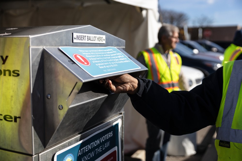 An election worker places a ballot in a drop-off box