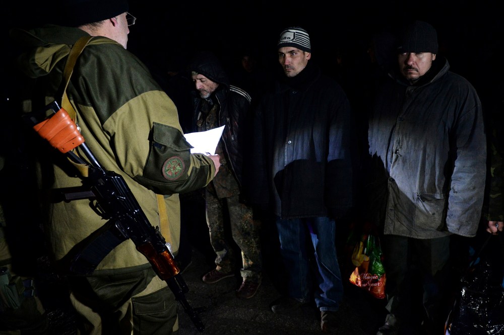 Ukrainian prisoners stand as a pro-Russian rebel holds a sheet of paper during procedures for a prisoner exchange with Ukraine on Dec. 26, 2014 in the eastern Ukrainian city of Yasinovataya, near Donetsk.