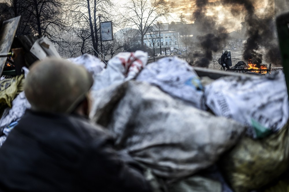 An anti-government protester looks at a protester adding tires to a fire at a barricade on February 21, 2014 in Kiev.