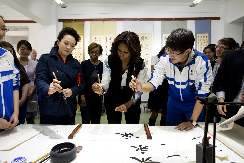 Peng Liyuan (L), wife of Chinese President Xi Jinping, shows First Lady Michelle Obama how to hold a writing brush as they visit a Chinese traditional calligraphy class at the Beijing Normal School, March 21, 2014 in Beijing, China.