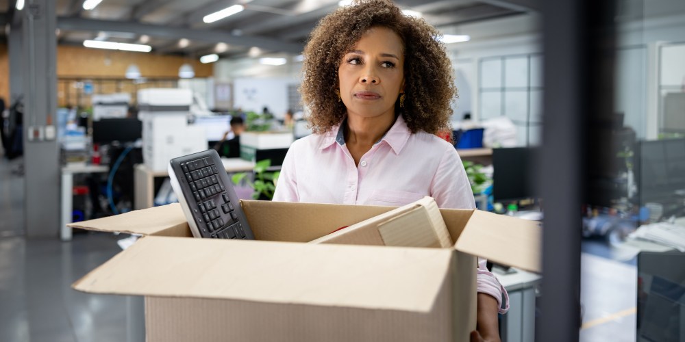 Business woman being fired from her office and carrying a box with her belongings