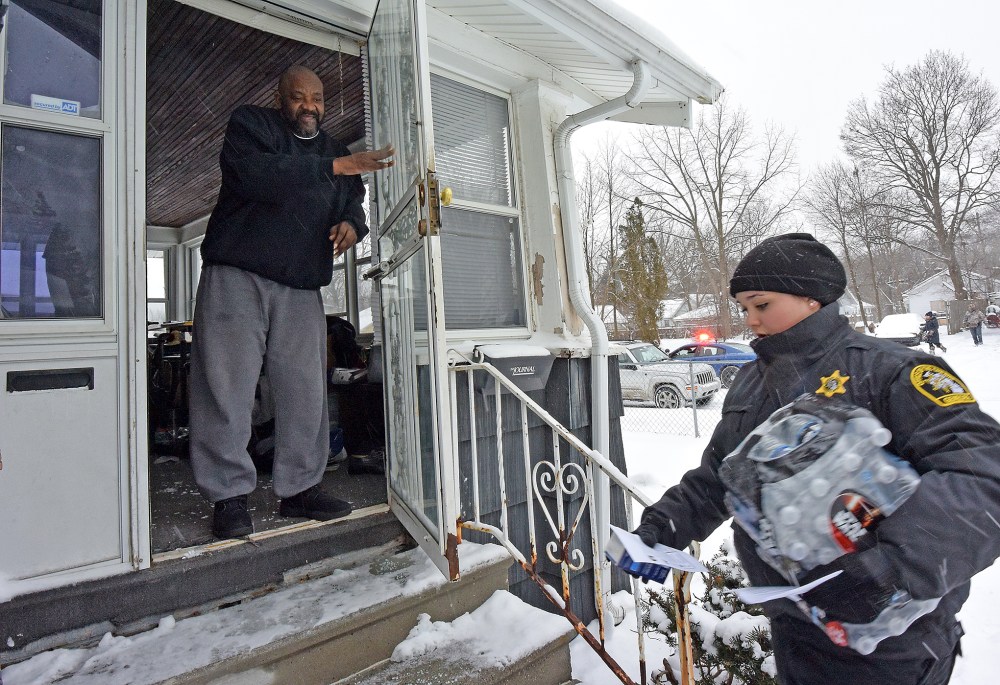 Samuel Smith receives a case of bottled water and a new water filter in Flint, Mich., as volunteers, Michigan State Police and Gennessee County Sheriff's Deputies deliver to residents, Jan 12, 2016. (Photo by Dale G. Young/The Detroit News/AP)