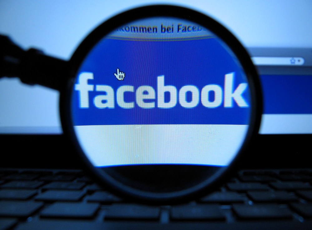 A magnifying glass is posed over a monitor displaying a Facebook page in Munich on Oct. 10, 2011. (Photo by Joerg Koch/AP)