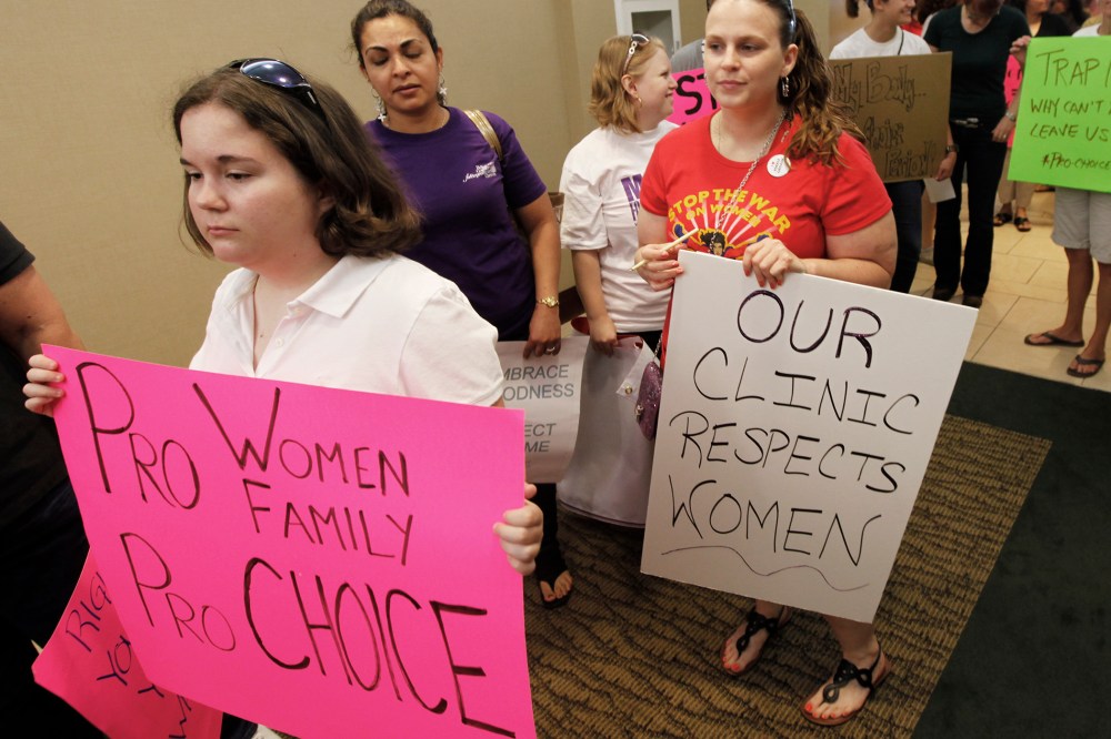 Protesters hold signs as they arrive for the start of a State Board of Health meeting in Richmond, Va.,  on June 15, 2012.