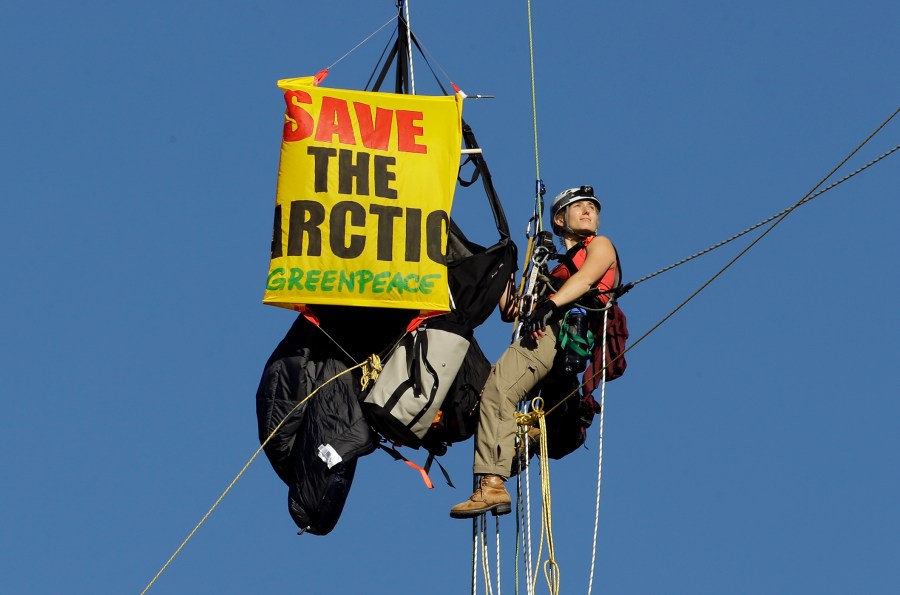 An activist looks towards the rising sun as she hangs from the St. Johns bridge as part of a protest to block the Royal Dutch Shell PLC icebreaker Fennica from leaving for Alaska in Portland, Ore., July 30, 2015. (Photo by Don Ryan/AP)
