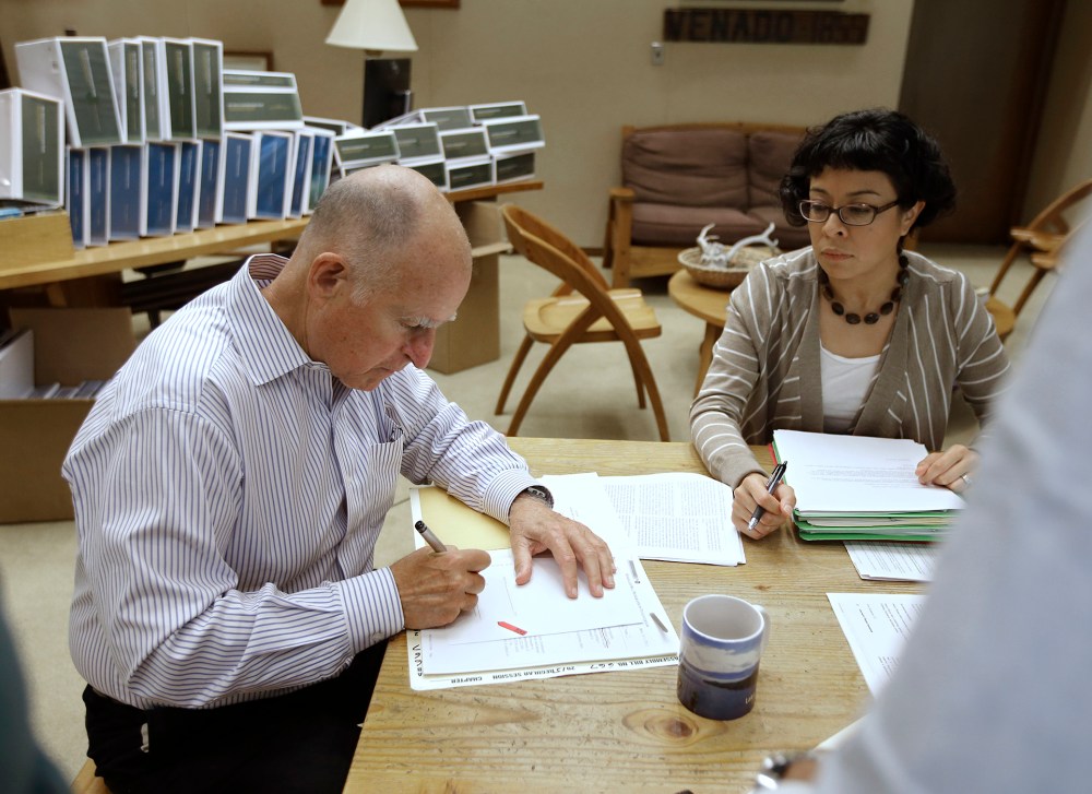 California Gov. Jerry Brown signs one of the hundreds of bills he has left to deal with as Garciela Castillo-Krings, his deputy legislative secretary, looks on at his Capitol office in Sacramento, Calif., Oct. 9, 2015. (Photo by Rich Pedroncelli/AP)