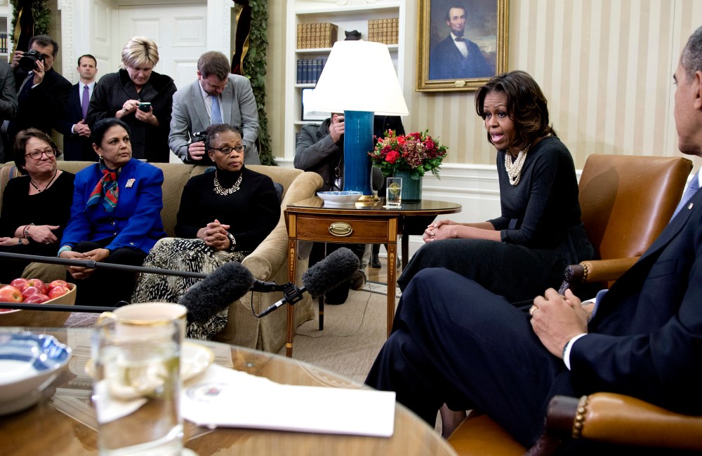 First Lady Michelle Obama speaks to the media as President Barack Obama listens as they meet with a group of mothers in the Oval Office of the White House in Washington, Dec. 18, 2013.