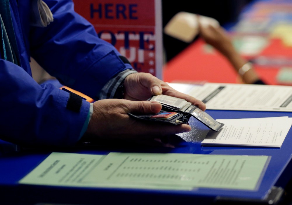 In this Wednesday, Feb. 26, 2014 photo, a voter shows his photo identification to an election official at an early voting polling site, in Austin, Texas.