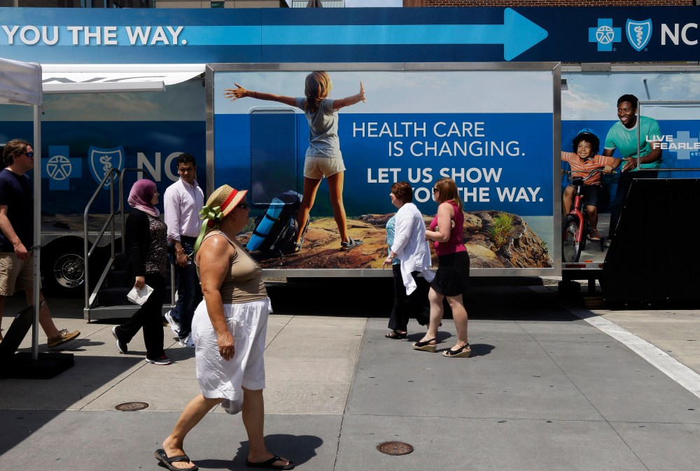 Pedestrians pass by a Blue Cross Blue Shield of North Carolina trailer at the downtown farmer's market in Raleigh, N.C., July 17, 2013.