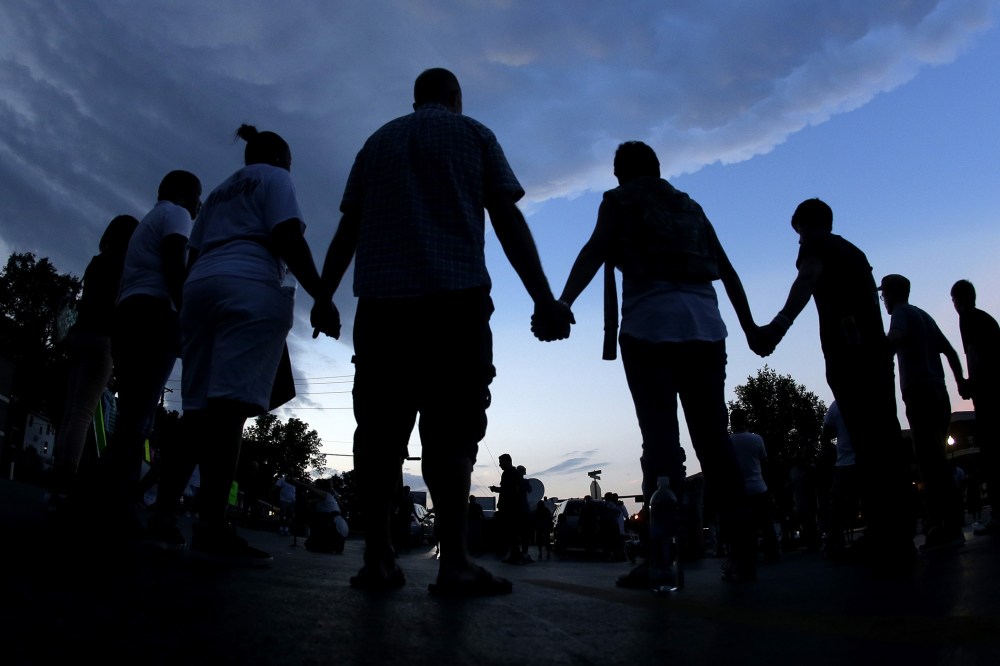 In this Aug. 20, 2014 fill photo people stand in prayer after march in Ferguson, Mo., to protest the shooting of Michael Brown. (Photo by Charlie Riedel/AP)