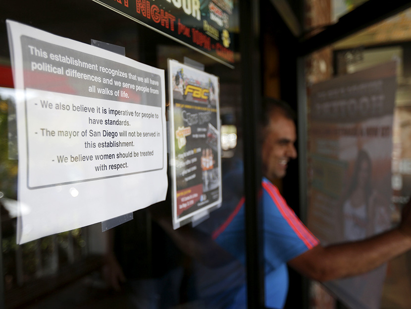 A man passes a sign, left,  posted on the outside of the entrance to a Hooters restaurant stating that San Diego Mayor Bob Filner will not be served Tuesday, Aug. 13, 2013, in San Diego. (Photo by Gregory Bull/AP)