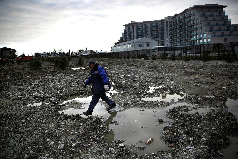 A construction worker steps over a puddle in a lot being prepared to be turned into a grassy lawn on Feb. 6, 2014, in Sochi, Russia.