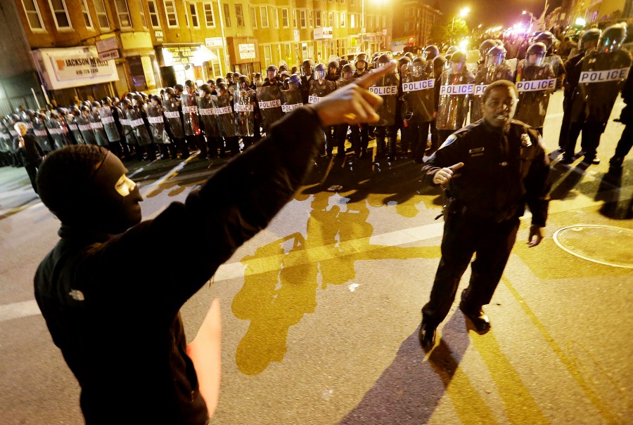 A protester at left argues with a policeman as police line up in riot gear in the background after a 10 p.m. curfew went into effect, April 30, 2015, in Baltimore. (Photo by David Goldman/AP)