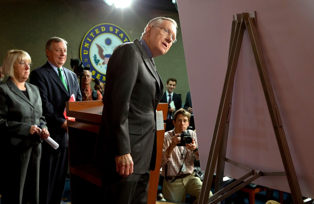 Senate Majority Leader Harry Reid of Nev., right, looks at a placard during a news conference in Washington, on Nov. 21, 2013