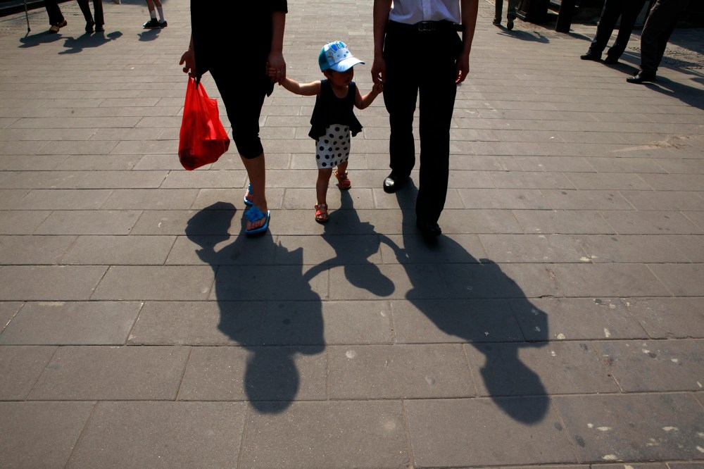 A couple hold hands with a child along a retail street in Beijing, China. (Photo by Ng Han Guan/AP)