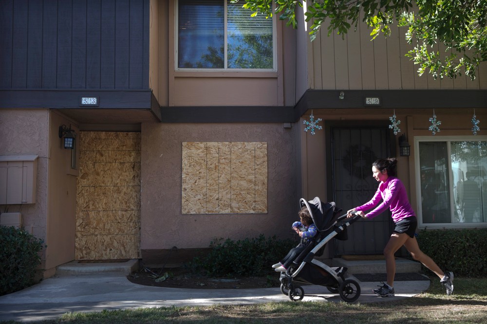 A woman pushes a baby stroller past the boarded-up townhouse rented by San Bernardino shooting rampage suspects Syed Farook and his wife, Tashfeen Malik, Saturday, Dec. 5, 2015, in Redlands, Calif. (Photo by Jae C. Hong/AP)