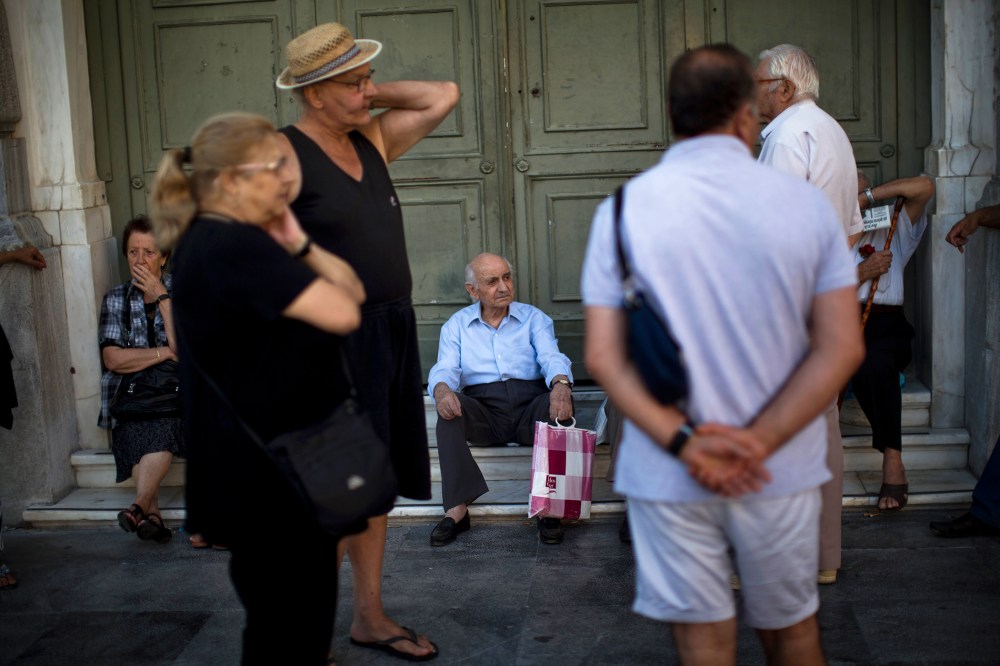 Pensioners sit at the main gate of the national bank of Greece as they wait to withdraw a maximum of 120 euros ($134) for the week in central Athens, July 13, 2015. (Photo by Emilio Morenatti/AP)