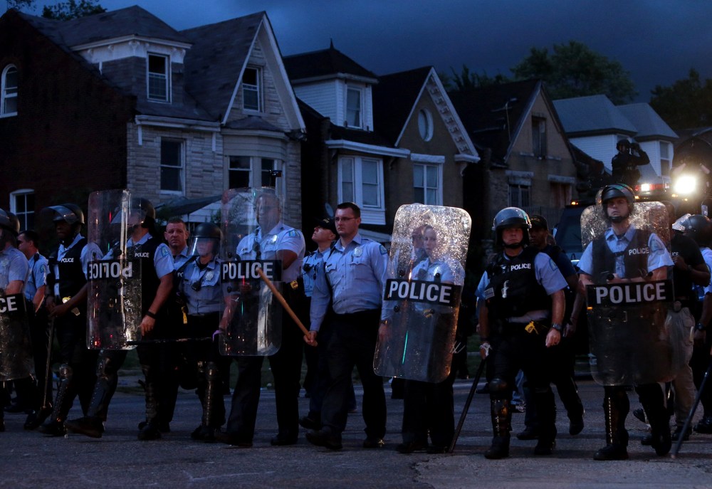 Police stand guard as protesters gather, Aug. 19, 2015, in St. Louis after a black 18-year-old fleeing from officers serving a search warrant was fatally shot after police say he pointed a gun at them. (Photo by Laurie Skrivan/St. Louis Post-Dispatch/AP)