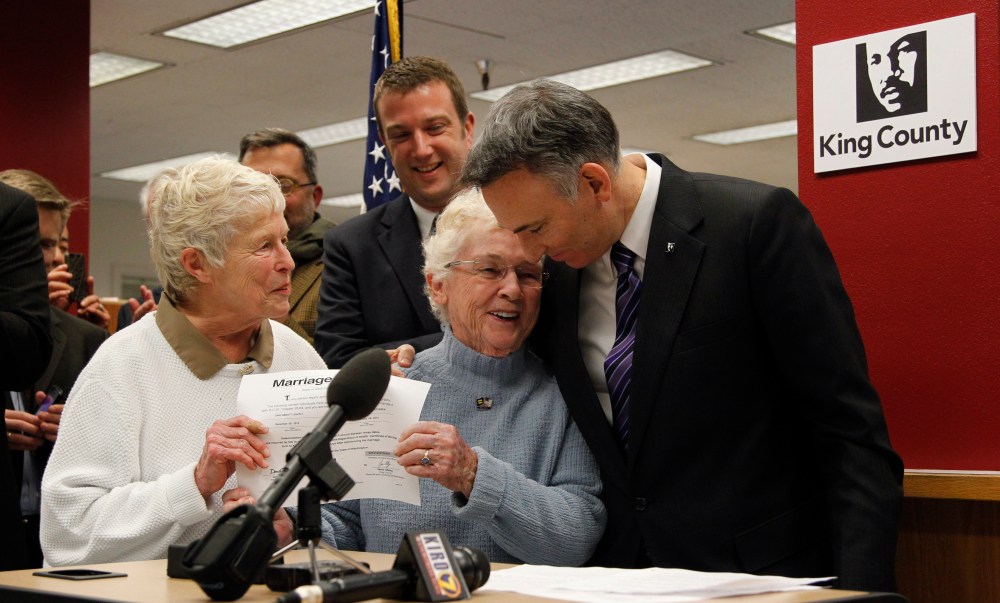 King County Executive Dow Constantine, right, leans down to embrace Pete-e Petersen as her partner, Jane Abbott Lighty, watches after Constantine issued them the first marriage license to a same-sex couples in Seattle. (AP Photo/Elaine Thompson)