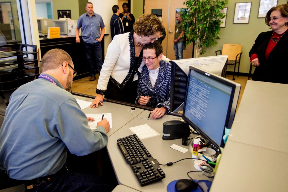 Suzanne Bryant, left, and Sarah Goodfreind hug as recording specialist Michael Mitchell for the Travis county clerk's office records the final paper work of their marriage certificate. (Photo by Ricardo B. Brazziell/Austin American-Statesman/AP)