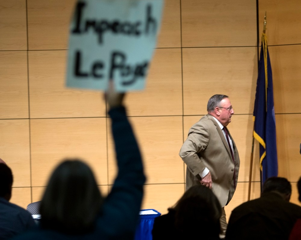 Gov. Paul LePage brings his town hall tour to Portland, speaking at the Abromson Center at the University of Southern Maine on Dec. 8, 2015. An audience member holds up a sign as LePage leaves the room. (Photo by Derek Davis/Portland Press Herald/Getty)