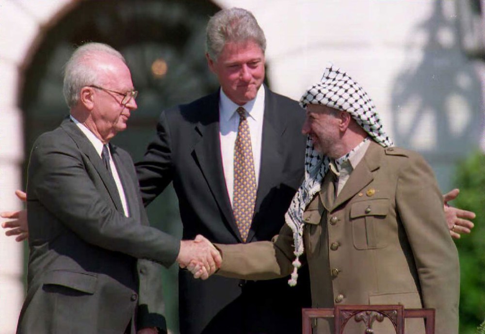 US President Bill Clinton stands between PLO leader Yasser Arafat and Israeli Prime Minister Yitzahk Rabin as they shake hands on Sep. 13, 1993 at the White House in Washington DC. (Photo by J. David Ake/AFP/Getty)