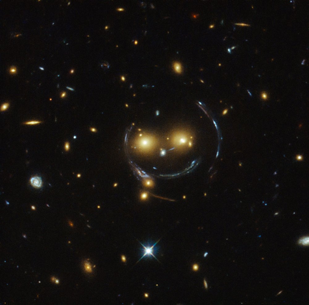In the case of this "happy face," the two eyes are the galaxies SDSSCGB 8842.3 and SDSSCGB 8842.4 and the misleading smile lines are actually arcs caused by an effect known as strong gravitational lensing. February 9, 2015