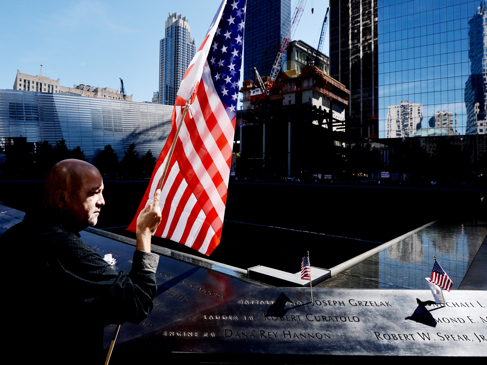 NEW YORK - SEPTEMBER 11:  Marshall Rodriguez of New York holds an American flag at the edge of the South Pool while visiting the names of friends he lost during memorial ceremonies for the eleventh anniversary of the terrorist attacks on lower...