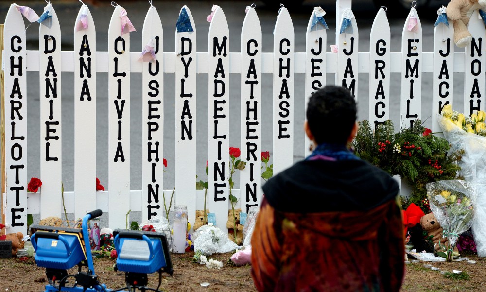 On Dec. 21, 2012 a woman kneels in front of a fence with the names of the 20 children killed in the school shooting at Sandy Hook Elementary School in Newtown, Conn.