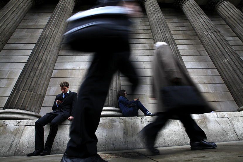 A man and woman use their mobile phones as commuters walk past the columns of the Bank of England in the City of London, July 3, 2012. (Photo by Andrew Winning/Reuters)