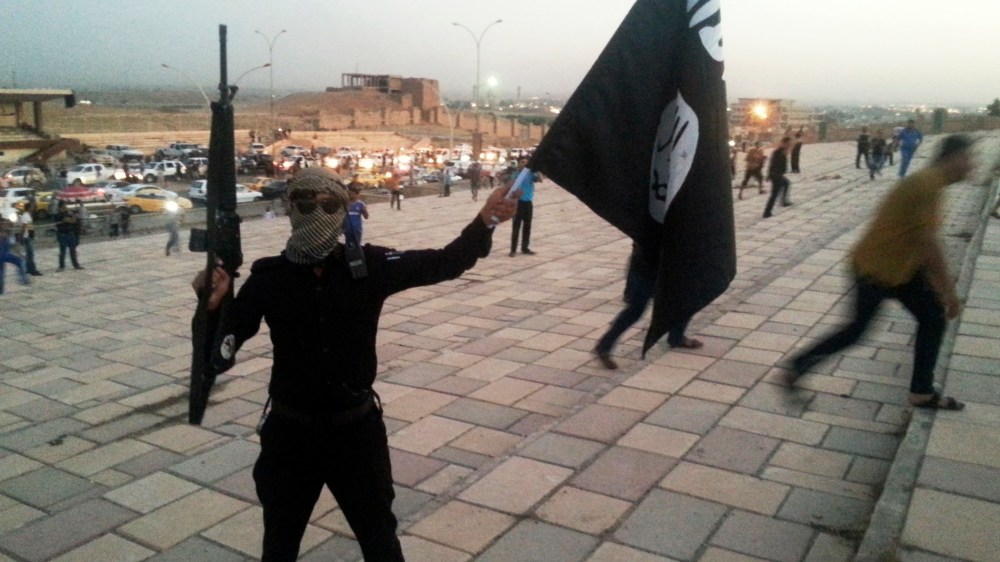 A fighter of the ISIL holds a flag and a weapon on a street in Mosul