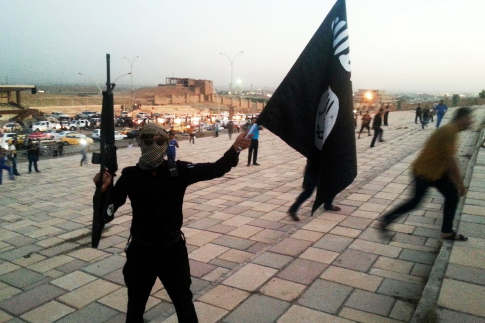 A fighter of the Islamic State of Iraq and the Levant (ISIL) holds an ISIL flag and a weapon on a street in the city of Mosul, June 23, 2014.