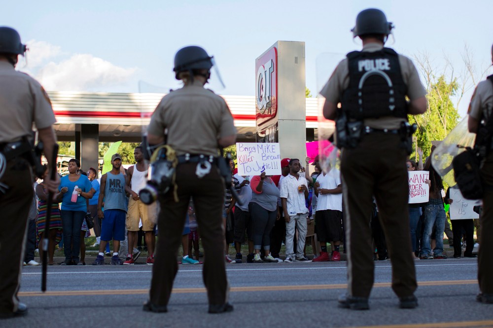 Police officers watch as demonstrators protest the death of black teenager Michael Brown in Ferguson, Missouri Aug. 12, 2014.