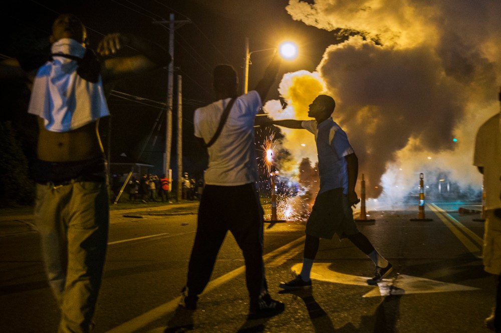Protesters involved with a more vocal and confrontational group of demonstrators stand and gesture as tear gas is fired, at further protests in reaction to the shooting of Michael Brown near Ferguson, Missouri August 18, 2014.