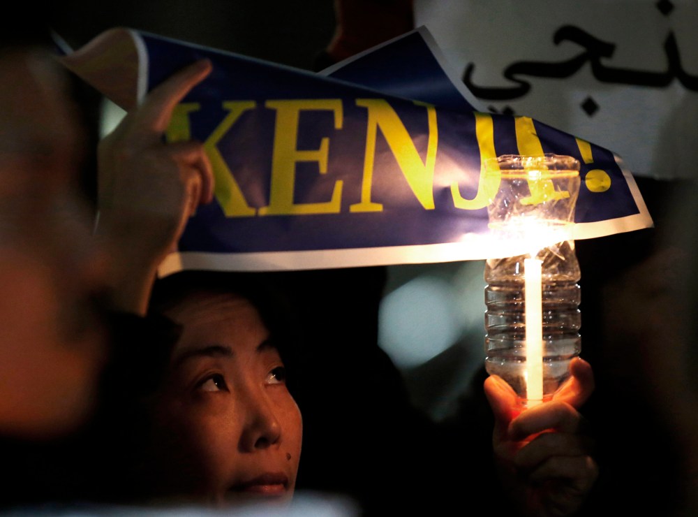A woman holding a candle and placard takes part in a vigil in front of Prime Minister Shinzo Abe's official residence in Tokyo, Jan. 30, 2015. (Photo by Toru Hanai/Reuters)