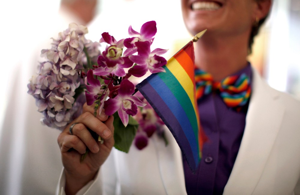 A woman holds a rainbow flag with her bouquet before getting married to her fiancee in West Hollywood, California, July 1, 2013.