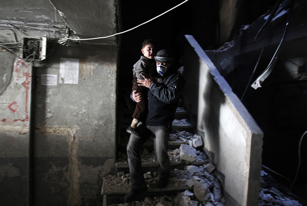 A man wearing a mask holds a child who was rescued at a site hit by what activists said were barrel bombs dropped by government forces, Jan. 31, 2014, in the Al-Ansari neighborhood of Aleppo, Syria.