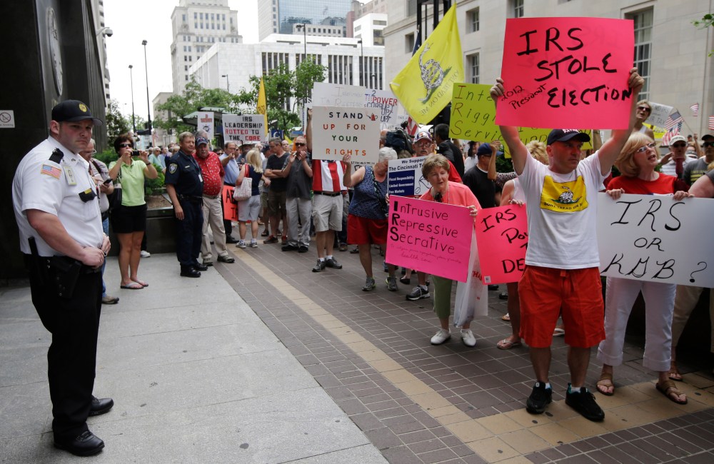 A federal officer watches as tea party activists demonstrate outside the John Weld Peck Federal Building, Tuesday, May 21, 2013, in Cincinnati. The building houses the main offices for the Internal Revenue Service in the city and is tied to the...